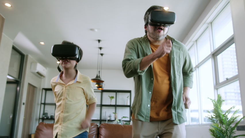 asian family Dad and son wear VR or virtual reality glasses,headsets standing and playing a video game at living room in  front of TV at home in quarantine period technology and innovation concept - Powered by Shutterstock - Get 15% off with code: PIKWIZARD15