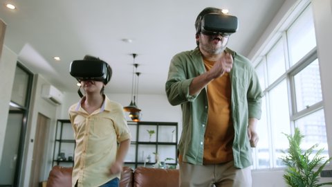 asian family Dad and son wear VR or virtual reality glasses,headsets standing and playing a video game at living room in  front of TV at home in quarantine period technology and innovation concept