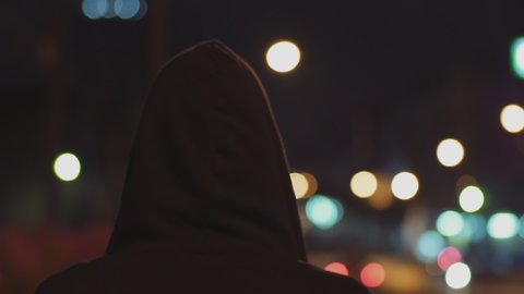 Closeup following shot of a man wearing a black jacket, with his hoodie up and his back behind the camera as he walks toward a deserted neighborhood