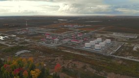 A video was shot from a great height. The weather is cloudy. Oil and gas field. Inside there are industrial buildings with red roofs and eight above-ground steel silos for storing petroleum products.