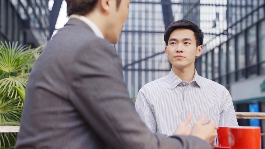 two asian business men sitting talking discussing in outdoor coffee shop Royalty-Free Stock Footage #1069015081