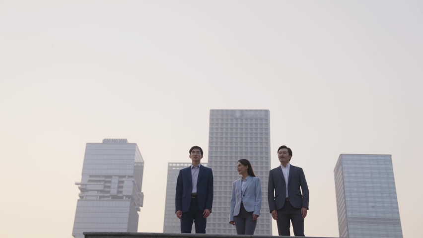 team of three asian business people celebrating success by jumping with modern city skyline in background Royalty-Free Stock Footage #1069015084