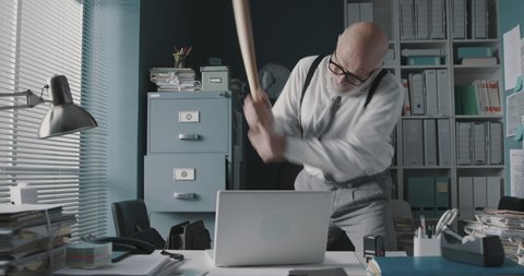 Stressed angry businessman smashing his laptop with a baseball bat, job burnout concept