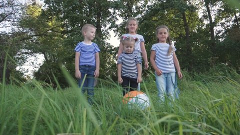 A happy family of children run in a group to the Park and play with an inflatable ball. Kids kick and catch up with a colored ball. Girls and a boy in a team compete for a toy. Teamwork