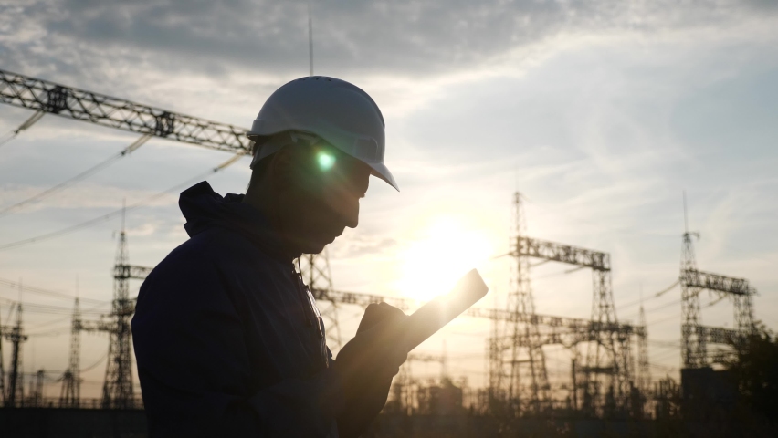 electrical silhouette worker engineer a working with digital tablet, near tower with electricity. energy business technology industry concept. electrical studying reading power documents on tablet Royalty-Free Stock Footage #1069016554