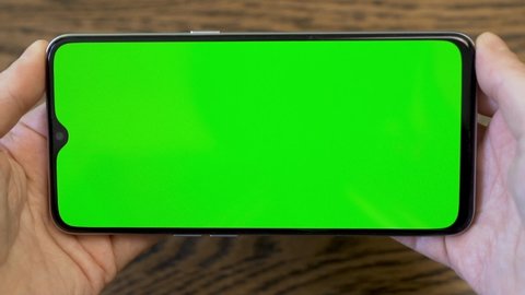 Close-up of a Horizontal Phone with a Green Screen Green Background in the Hands of A Person. Video Conferences, Video Content, Blank, Advertising, A Place to Advertise Your Business.