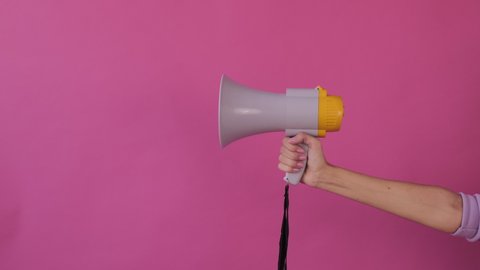 attention! Woman hand with megaphone appears the frame to right on pink background  