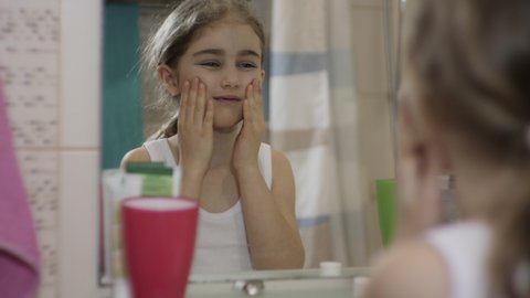 Portrait Young Funny Little Girl Enjoying Making Grimace in Bathroom Looking at Mirror Reflection. Happy Portrait Cute Caucasian Toothless Child Making Grimace Face in Bathroom. Funny Emotion Child.