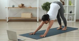 Happy motivated millennial indian ethnicity sporty woman watching online yoga training, repeating complex of asana, stretching muscles, involved in workout or distant fitness class alone at home.