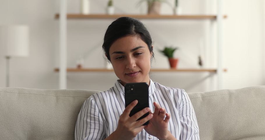 Unhappy 25s young indian biracial woman reading message with unpleasant news, feeling stressed of bad device work or interrupted unstable internet connection, using smartphone sitting on sofa at home. Royalty-Free Stock Footage #1069025461