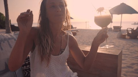 Woman having a cocktail at sunset on tropical beach