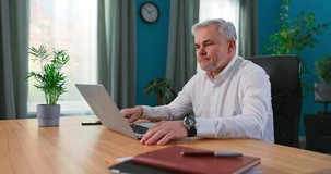 Mature 55s couple in separation talk during virtual meeting by video call. Grey haired husband enjoy conversation with wife remotely, older generation advanced users of video conference app and laptop