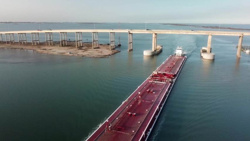 Aerial view of a large red barge moving along the Gulf Intercoastal Waterway and under JFK Memorial Causeway bridge into Laguna Madre; Corpus Christi Texas Royalty-Free Stock Footage #1069039105