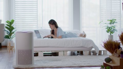 air purifier in bed room for clean dust and fresh air with woman lying on bed working with computer laptop and relax in background,Wellness of clean and fresh air for breathing and good health at home