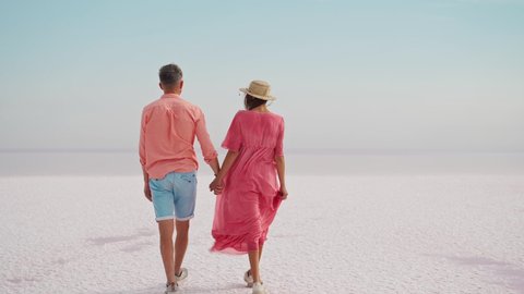 attractive young couple in pink wear walking holding hands on white salty coast of pink lake looks like desert. Romantic travel honeymoon vacation, traveling to amazing unusual places in Ukraine