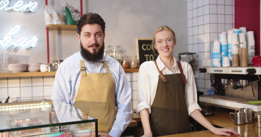 Portrait of friendly Caucasian bartenders working at urban coffee shop. Adult lady and guy standing behind bar, looking at camera, crossing arms and smiling. Business, entreprenuership concept.