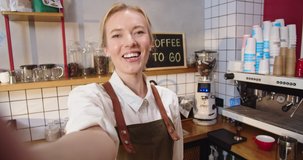 POV Successful Caucasian woman influencer in apron broadcasting from coffee shop. Adult female barista blogger influencer talking to her viewers, followers and speaking on camera. Vlog, social media.