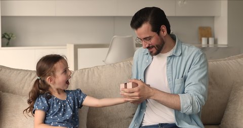 Caring little kid girl makes surprise, gives gift box to young daddy congratulates him Happy Father Day, dad feels deeply moved hugs small daughter. Family celebrate birthday and life events concept