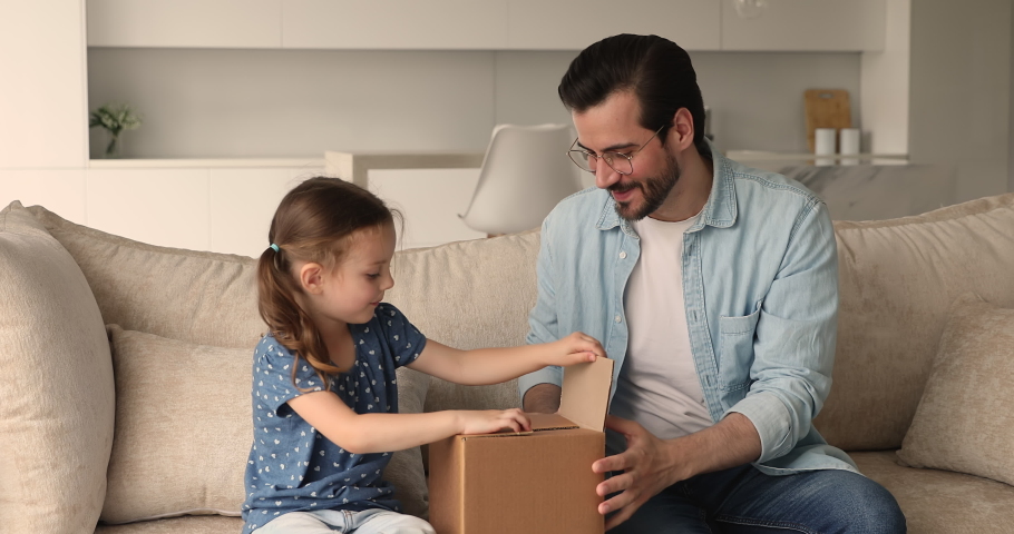Preschool girl sit on couch with loving dad, family open received parcel enjoy surprise, take out fluffy toy bear and gift box. Quick express delivery, e-commerce online services happy clients concept Royalty-Free Stock Footage #1069059400