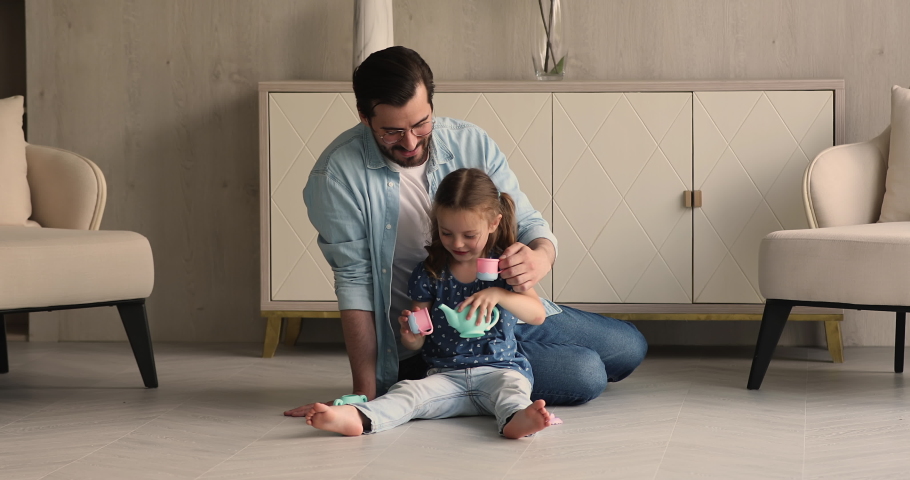 Dad play tea-party with little daughter, sit on warm floor in cozy living room hold toys set cups drink imaginary tea enjoy funny playtime together at modern home. Father Day celebration, fun concept Royalty-Free Stock Footage #1069059427