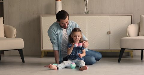 Dad play tea-party with little daughter, sit on warm floor in cozy living room hold toys set cups drink imaginary tea enjoy funny playtime together at modern home. Father Day celebration, fun concept