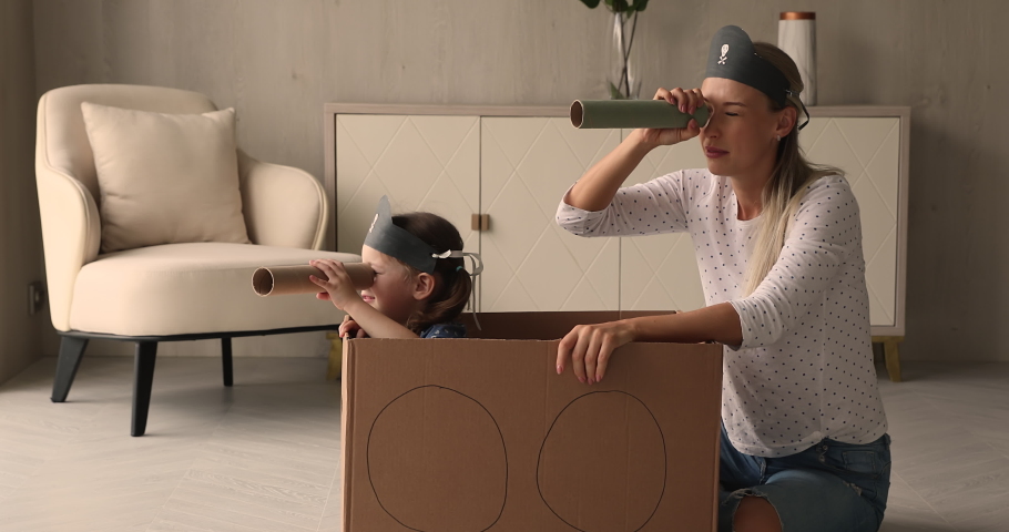 Little kid girl sit inside of carton box play pirates with mother, family holding paper tubes spyglasses watching into distance pretend be explorers. Funny playtime with children at home, fun concept Royalty-Free Stock Footage #1069059580