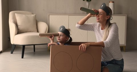 Little kid girl sit inside of carton box play pirates with mother, family holding paper tubes spyglasses watching into distance pretend be explorers. Funny playtime with children at home, fun concept