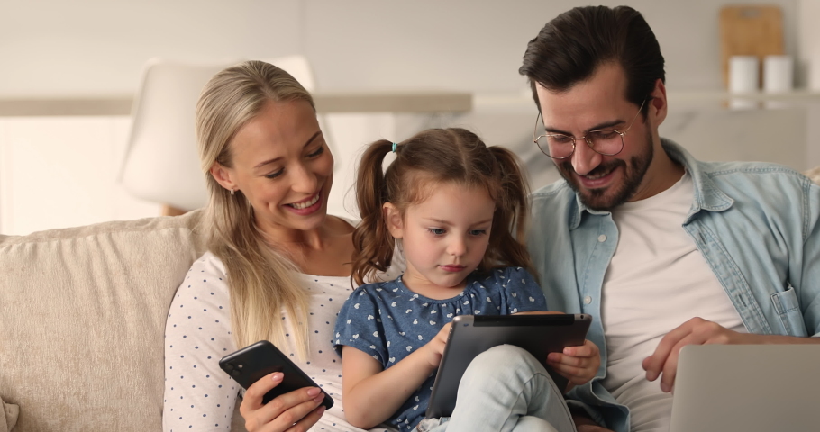 Addicted with modern gadgets family sit on sofa spend time together using diverse device. Small kid play videogame on tablet rest at home with parents holding phone and pc. Modern tech overuse concept Royalty-Free Stock Footage #1069059688
