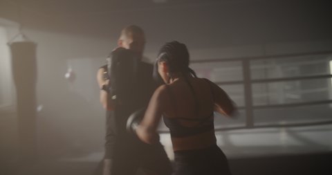 Young Woman Athlete and Caucasian Man Training in Haze on Boxing Ring. Sparring of Young Sportswoman and Personal Trainer in Backlight. Combat Sport, Lifestyle.