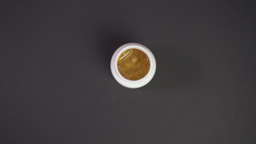 Close up woman s hand falls out Prescription bottle filled with yellow pills spills in to scatter contents. Yellow pills are spilling on the black medical table. Concept of healthcare and medicine 4k