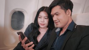 Asian Businessman and Businesswoman using smartphone together enjoying moment, Couple business team on the plane flight, Business class, Airplane concept. 4K UHD Footage.