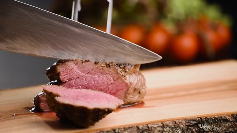 Man cut grilled steak with a sharp knife on wooden board
