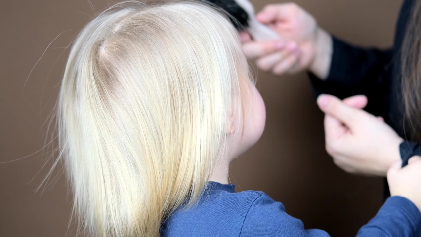 mom combing her daughter's hair, little blonde girl with a wooden brush with natural bristles, child and woman on a dark brown background, concept of hygiene, hair care, childhood, motherhood Royalty-Free Stock Footage #1069067266