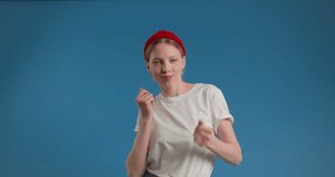 Young funny blond woman in white shirt dancing and smiling isolated over blue
