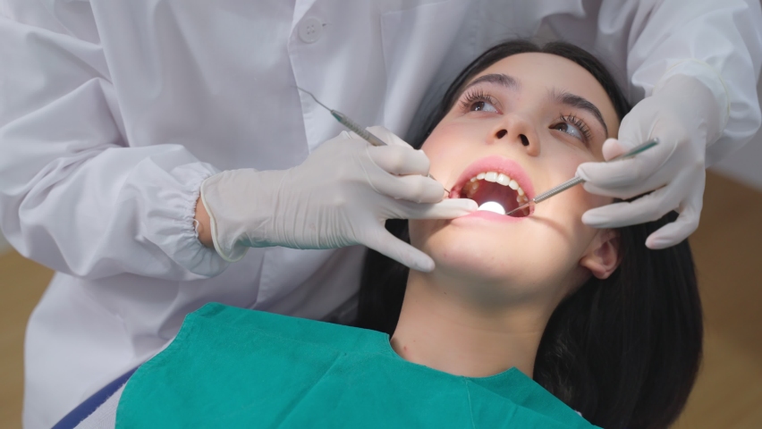Asian female dentist examining young girl patient's teeth at dental clinic. Doctor probing teeth with dental instrument using an explorer look for cavities treatment and checking problems with filling | Shutterstock HD Video #1069073473