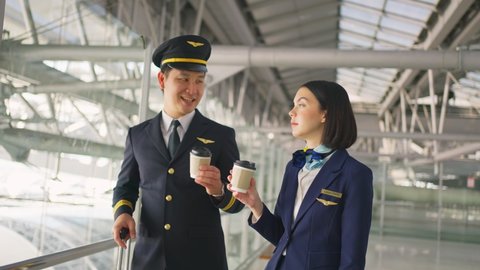 Asian airliner pilot and air hostess talking and drinking coffee together in airport terminal with smile face and happiness. Commercial cabin crew or hostress, airplane and pilot occupation concepts.