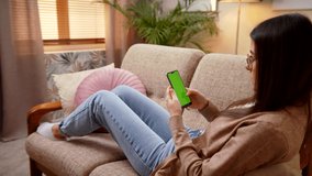 Caucasian Young Woman Lying On Sofa And Texting On Smart Phone Green Screen. Resting In Living Room Share Messages In Social Media, Chatting, Using Mobile Apps, Doing Shopping Leisure Time At Home