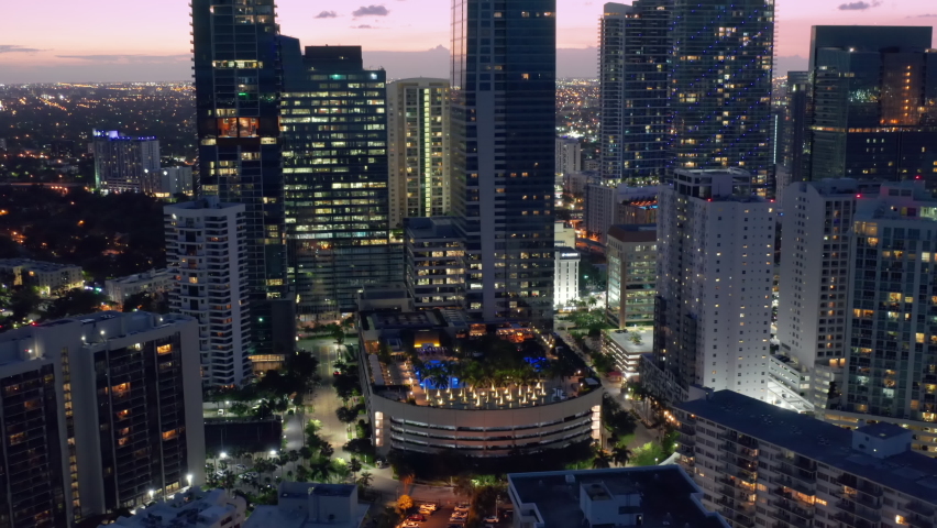 Downtown Miami at night, aerial. Modern urban cityscape, drone b roll 4K, travel footage. Cinematic top down view on rooftop bar with pool design landscape park with palm trees and multiple fireplaces.