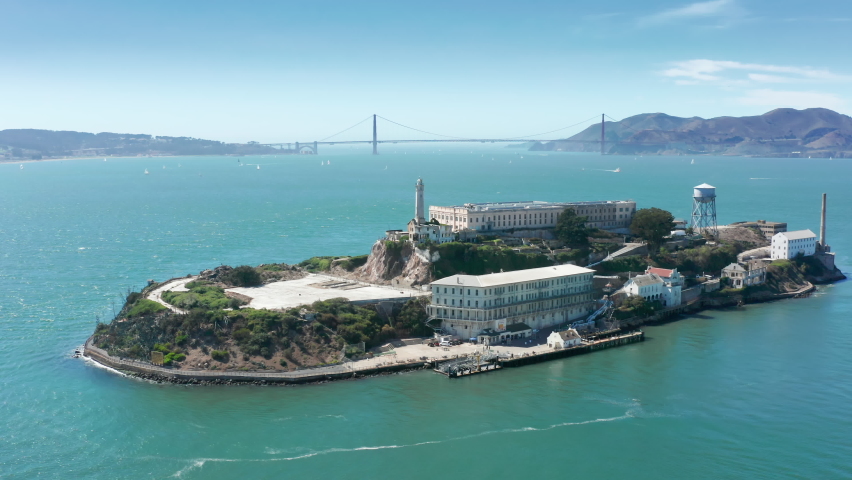 Aerial Alcatraz island with Golden Gate bridge on motion background. Historic prison building in green San Francisco bay area waters on summer day. World famous touristic landmarks and attraction 4K