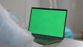 Close-up of chromakey laptop with unrecognizable doctor sitting at table talking. Professional Caucasian woman consulting online on coronavirus pandemic outbreak using video chat on green screen.