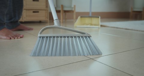 Slow motion shot of asian woman cleaning and sweeping dust on the floor with a broom and dustpan in the living room. Woman doing chores at home. Housekeeping concept.