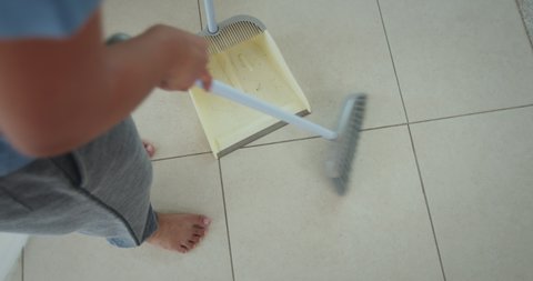 Slow motion shot of asian woman cleaning and sweeping dust on the floor with a broom and dustpan in the living room. Woman doing chores at home. Housekeeping concept.