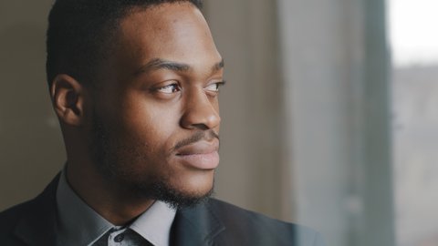Close-up black serious male face in profile, concentrated expression, portrait of pensive african american business man boss looking out window in office thinking making decision turns  head to camera