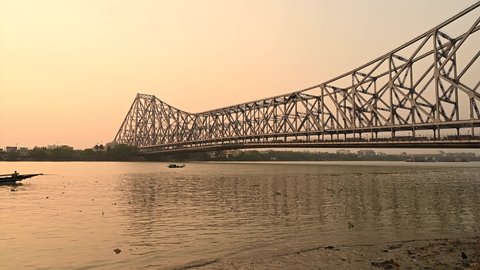 Silhouette of a fishing boat in River Ganges crossing Howrah Bridge at the time of sunset.