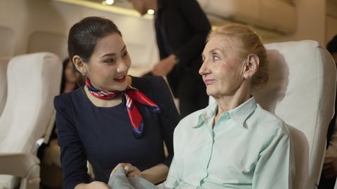 On the plane, Old female passengers on the plane were taken care of by Air hostess. Asian Cabin Crew covered senior with a blanket. Senior passengers smiling happily after talking with airline staff.