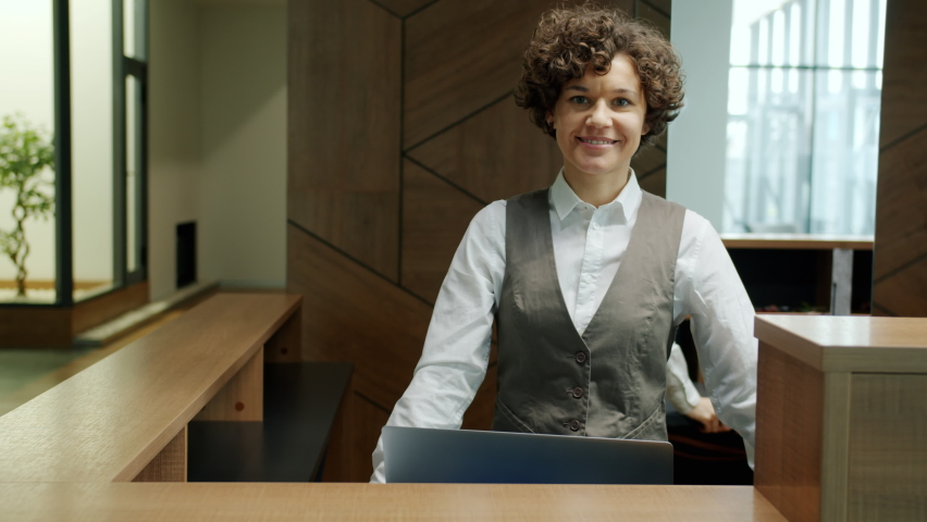 Portrait of attractive young woman in uniform standing at reception desk alone smiling looking at camera. Business locations and professions concept. Royalty-Free Stock Footage #1069109848