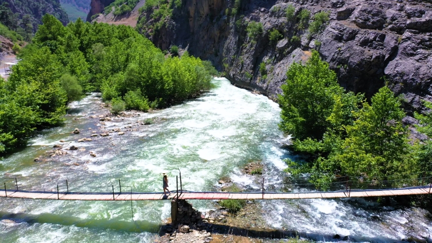 AERIAL. Young woman walking on the bridge above huge and strong river
