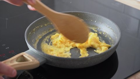 Scrambled eggs, omelette. Cooking breakfast with pan-fried eggs. Preparing food on pan. Mixing egg in pan with wooden spatula. Morning daily routine of weekend. Texture of omelet. Keto ketogenic diet