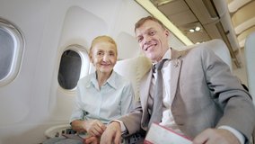 Sweet senior couple using cameras recording video clips on the plane, Exited couple waving hands greeting camera and smiling happily looking outside of windows of plane.