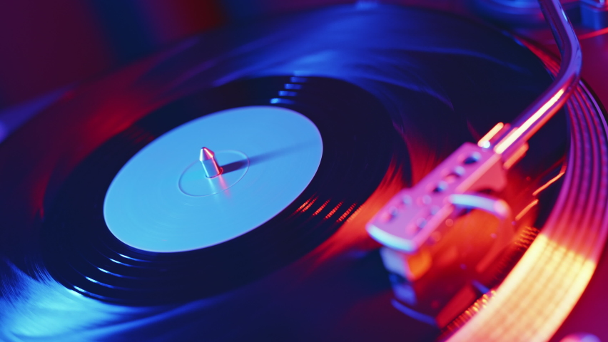 Vinyl Records Player turntable RGB Led of red and blue neon lights. Focus Needle slides smoothly on rotate  black vinyl record. Closeup on background. Rotating plate Top view. Disco 70s, 80s, 90s Royalty-Free Stock Footage #1069120429